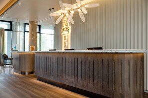 A modern reception desk with a wooden finish, a decorative light fixture above, and a view of the interior space.