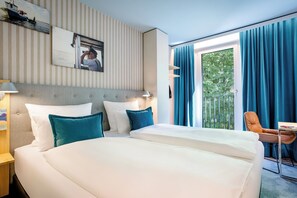 A hotel room with a large bed, a desk, a chair, and a view of greenery through the window.