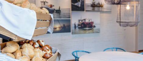 A wooden bread basket filled with various breads, a round table, and blue chairs in a room with nautical-themed wall art.