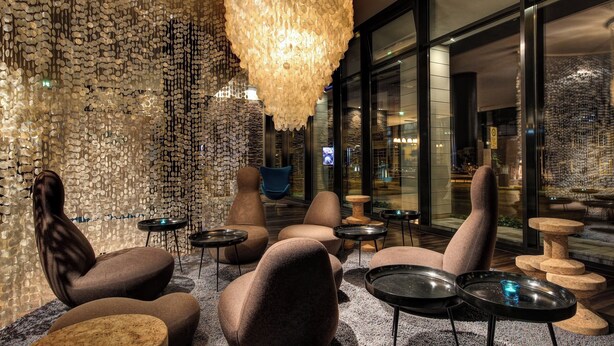 A modern lounge area with plush seating, a unique textured wall, and a hanging light fixture. - Motel One Rostock (Rostock)