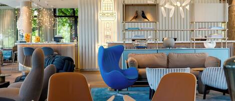 Un interior moderno con una zona de bar, asientos que incluyen una silla azul, y una estantería con objetos decorativos.