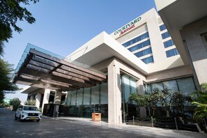 A Courtyard Marriott hotel with a modern glass facade, a covered entrance, and a parking area. - Courtyard by Marriott Pune Chakan (Rajgurunagar)