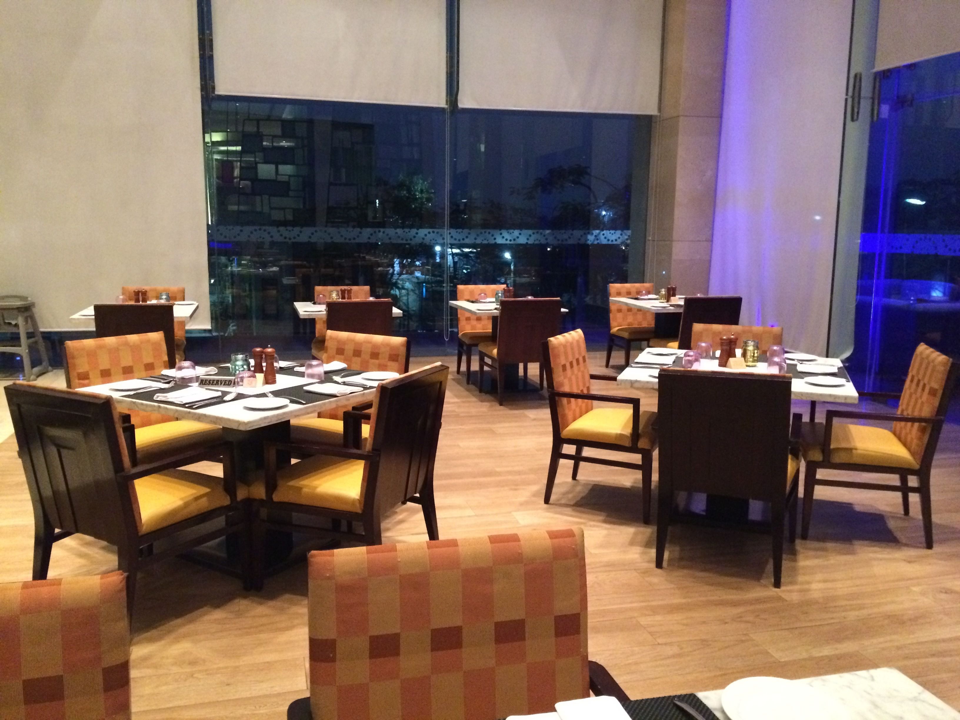 Ein Restaurant mit gedeckten Tischen, bequemen Stühlen und Blick auf die beleuchtete Stadt.