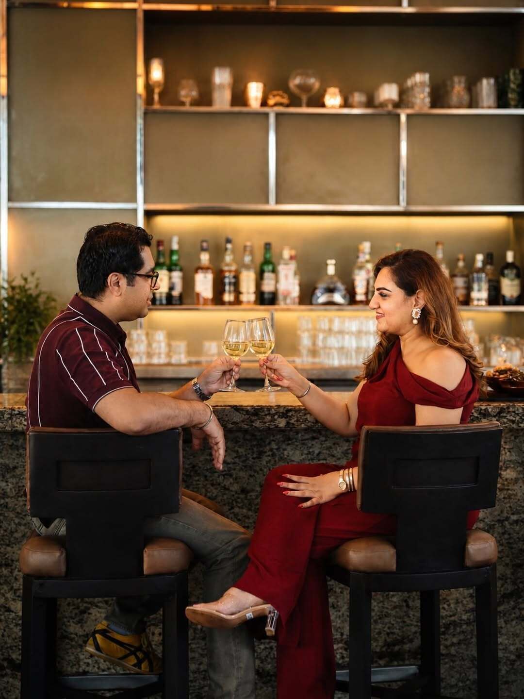 Two people seated at a bar with a backdrop of shelves stocked with bottles.