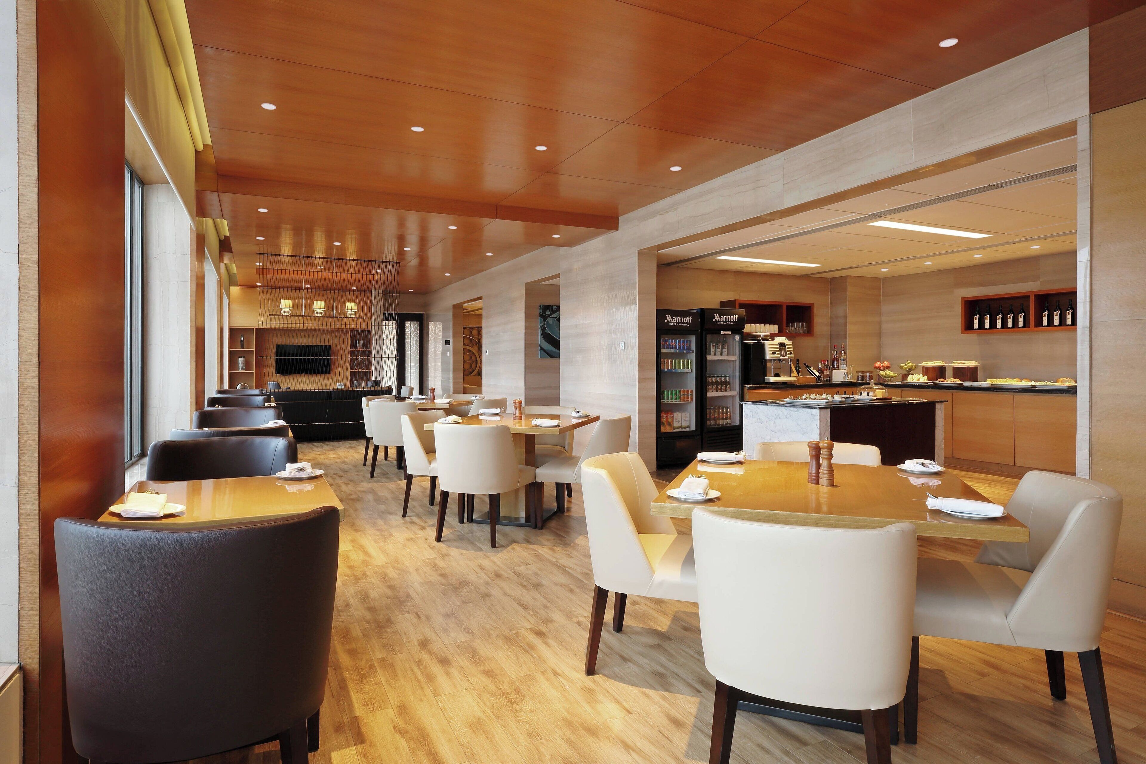 Een modern restaurantgedeelte in een hotel, met houten tafels en stoelen, een keukenhoek en een minibar.