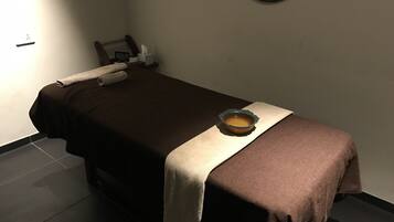 A single bed with a brown bedspread and a beige blanket, a small bowl of water, a tissue box, and a clock on the nightstand.