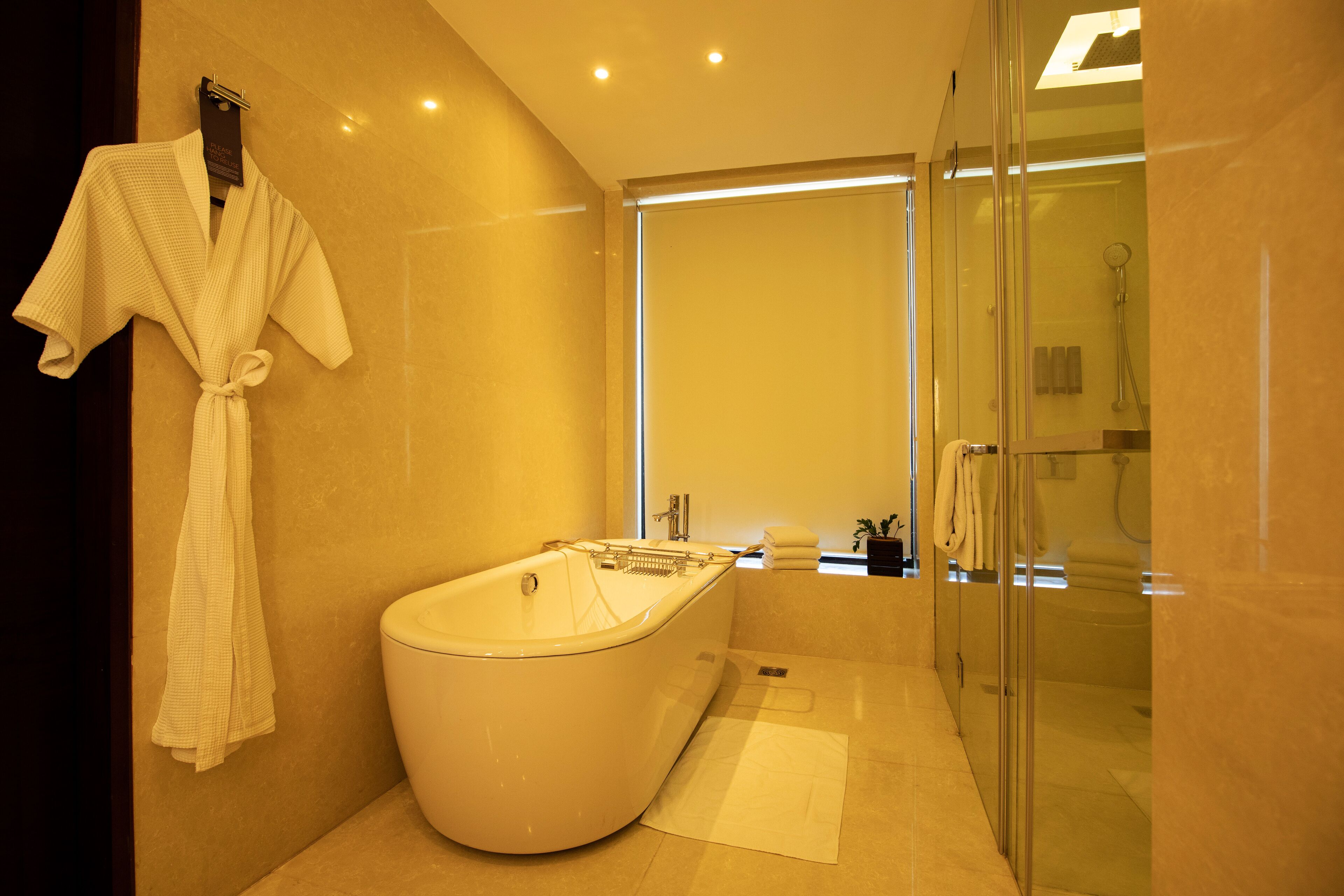 Een moderne badkamer met een vrijstaand bad, een douchecabine met glazen wanden en een handdoekrek met badjassen.