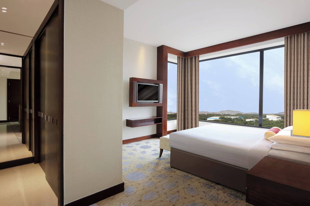 A hotel room with a large bed, a TV mounted on the wall, and a view of the landscape through the window.
