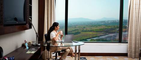 A hotel room with a large window offering a view of a cityscape and mountains.