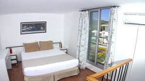 A bedroom with a bed, bedside tables, a window with curtains, a view of the outside, and an air conditioning unit. - Vela Apart Hotel (Cesme)