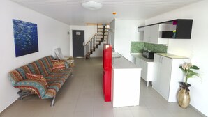 A modern living room with a sofa, a staircase leading to a kitchen, and a dining area. - Vela Apart Hotel (Cesme)