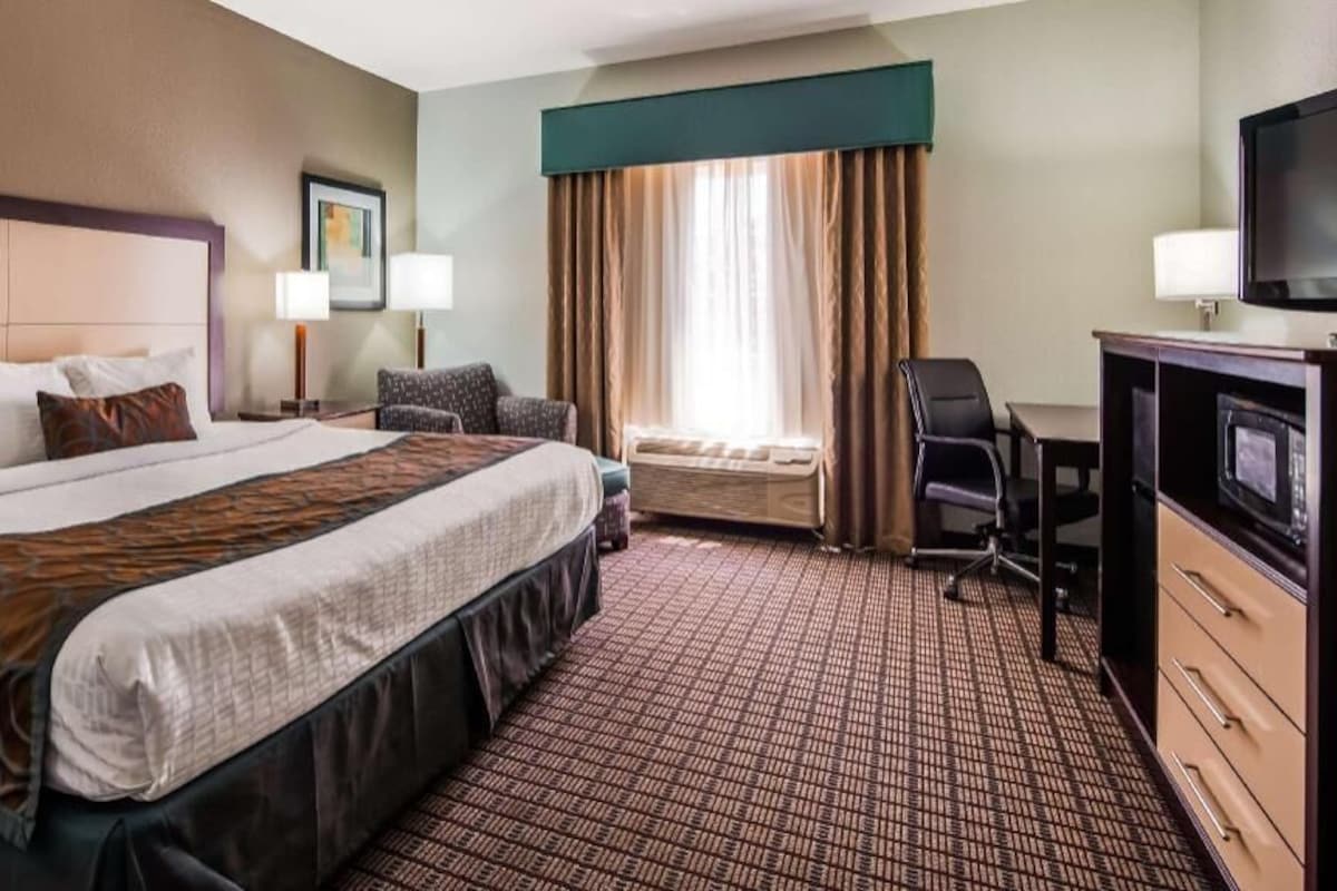 A hotel room with a large bed, a desk with a TV, a chair, and a window with curtains.
