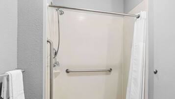 A glass-enclosed shower with a handrail, a towel rack, and a white shower curtain.