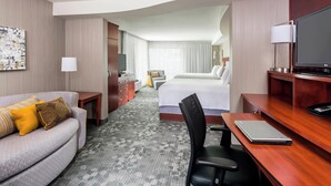 Ein Hotelzimmer mit Sofa, Schreibtisch mit Laptop, Bett, Fernseher und TV-Schrank.