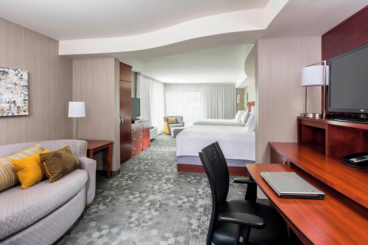 A hotel room with a sofa, a desk with a laptop, a bed, a TV, and a TV stand.