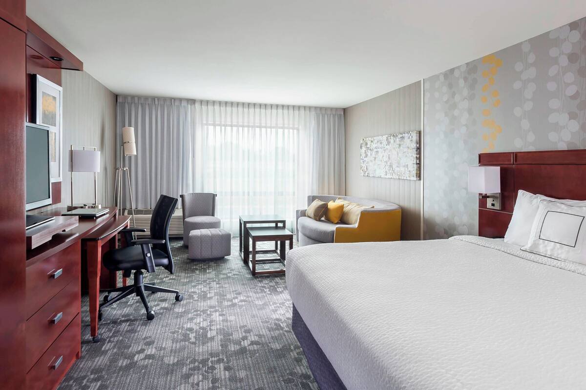 A hotel room with a large bed, a desk with a computer, a chair, a sofa, and a small table.