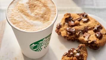 Una taza de Starbucks con una bebida espumosa y una galleta con chispas de chocolate.