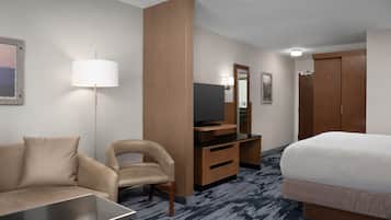 A hotel room with a bed, a sofa, a desk, a television, a mirror, and a wardrobe.