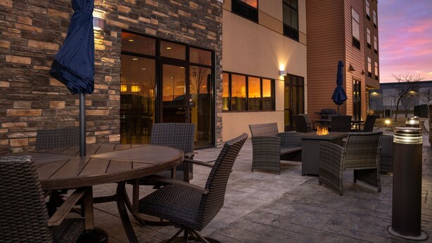 An outdoor patio with a round table and wicker chairs, a fire pit, and a brick wall.