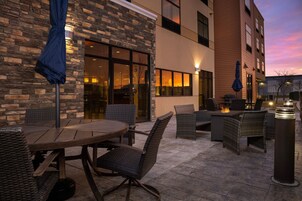 Un patio al aire libre con una mesa redonda y sillas de mimbre, un brasero y una pared de ladrillo.