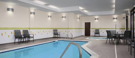 Una piscina con sillas y mesas, rodeada de muros con iluminación empotrada y suelo de baldosas.