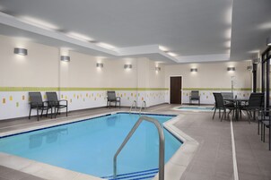 A swimming pool with chairs and tables, surrounded by walls with recessed lighting and a tiled floor.