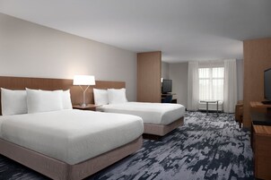 A hotel room with two beds, a desk, a TV, and a window with curtains.