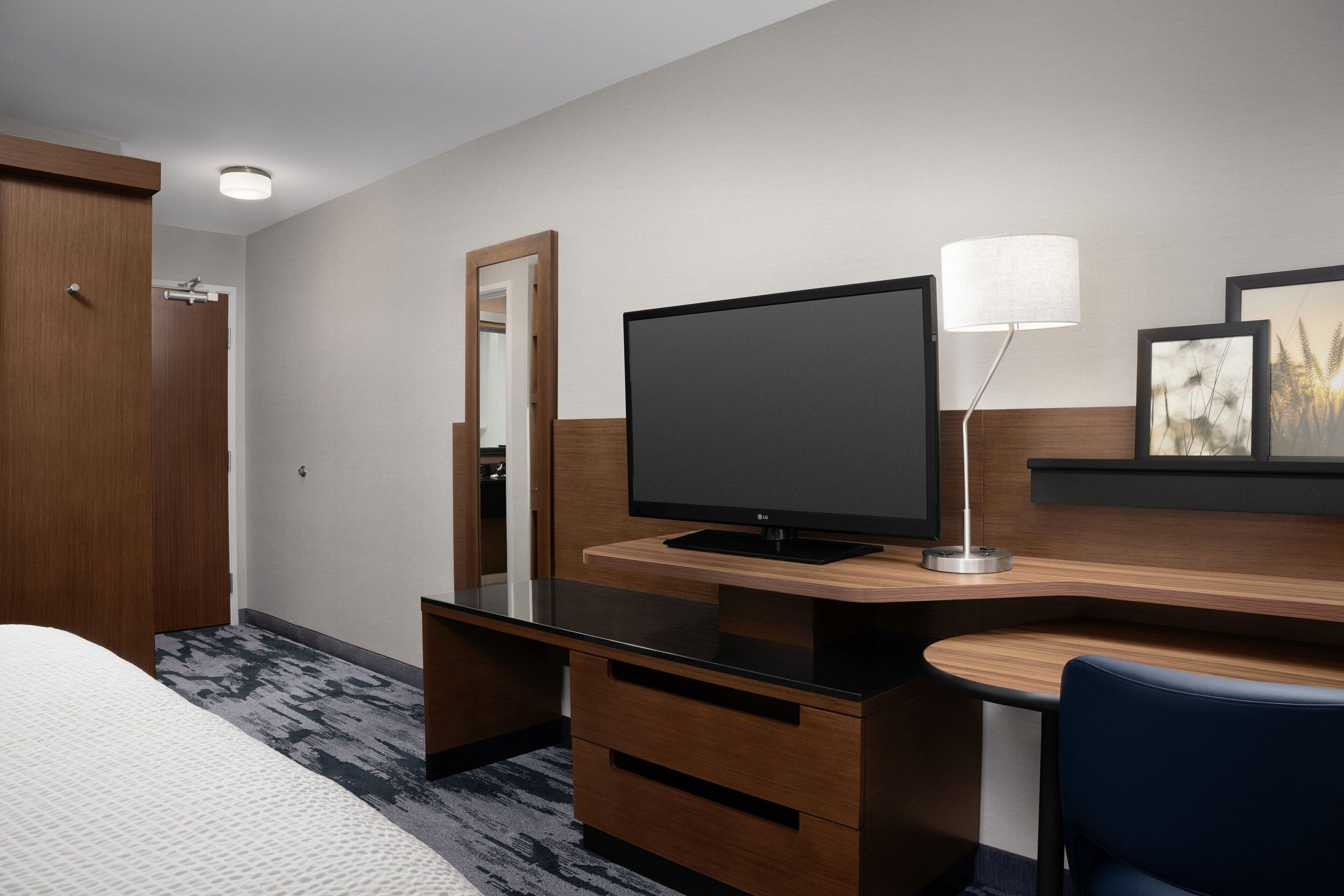 Habitación de hotel con cama, escritorio, televisor de pantalla plana, lámpara y espejo.