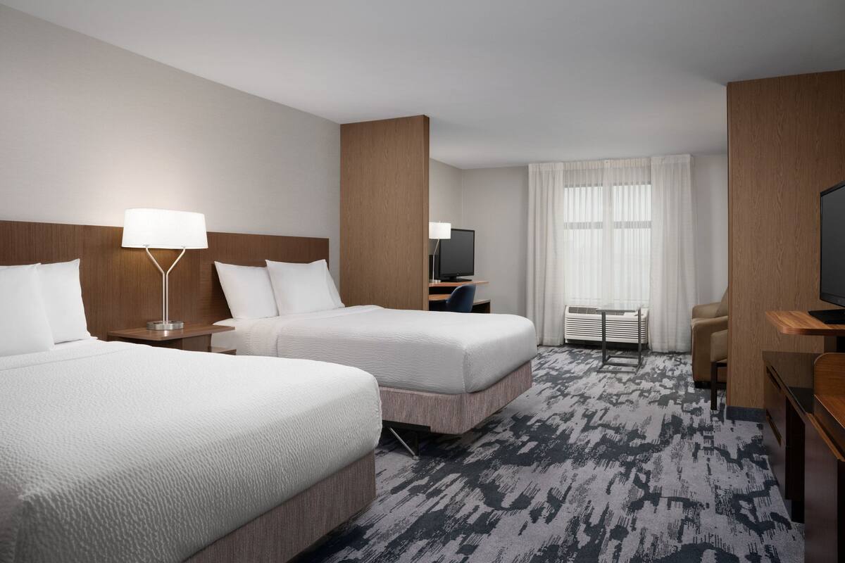A hotel room with two beds, a desk, a television, and a window with curtains.