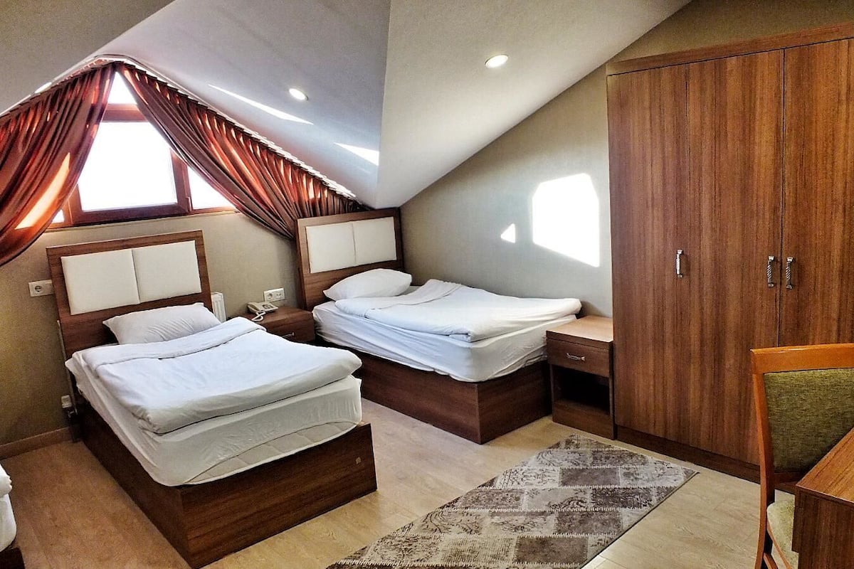 A bedroom with two beds, a wooden wardrobe, a desk, and a television.