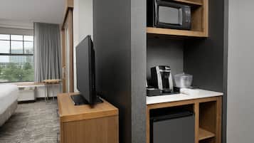 A hotel room with a bed, a TV on a wooden stand, a microwave, a coffee maker, and a mini fridge.