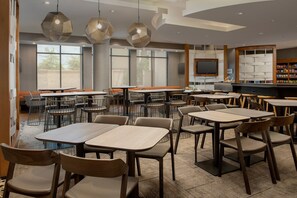 A modern dining area with multiple tables and chairs, large windows, and a television. - SpringHill Suites Jackson North/Ridgeland (Ridgeland)