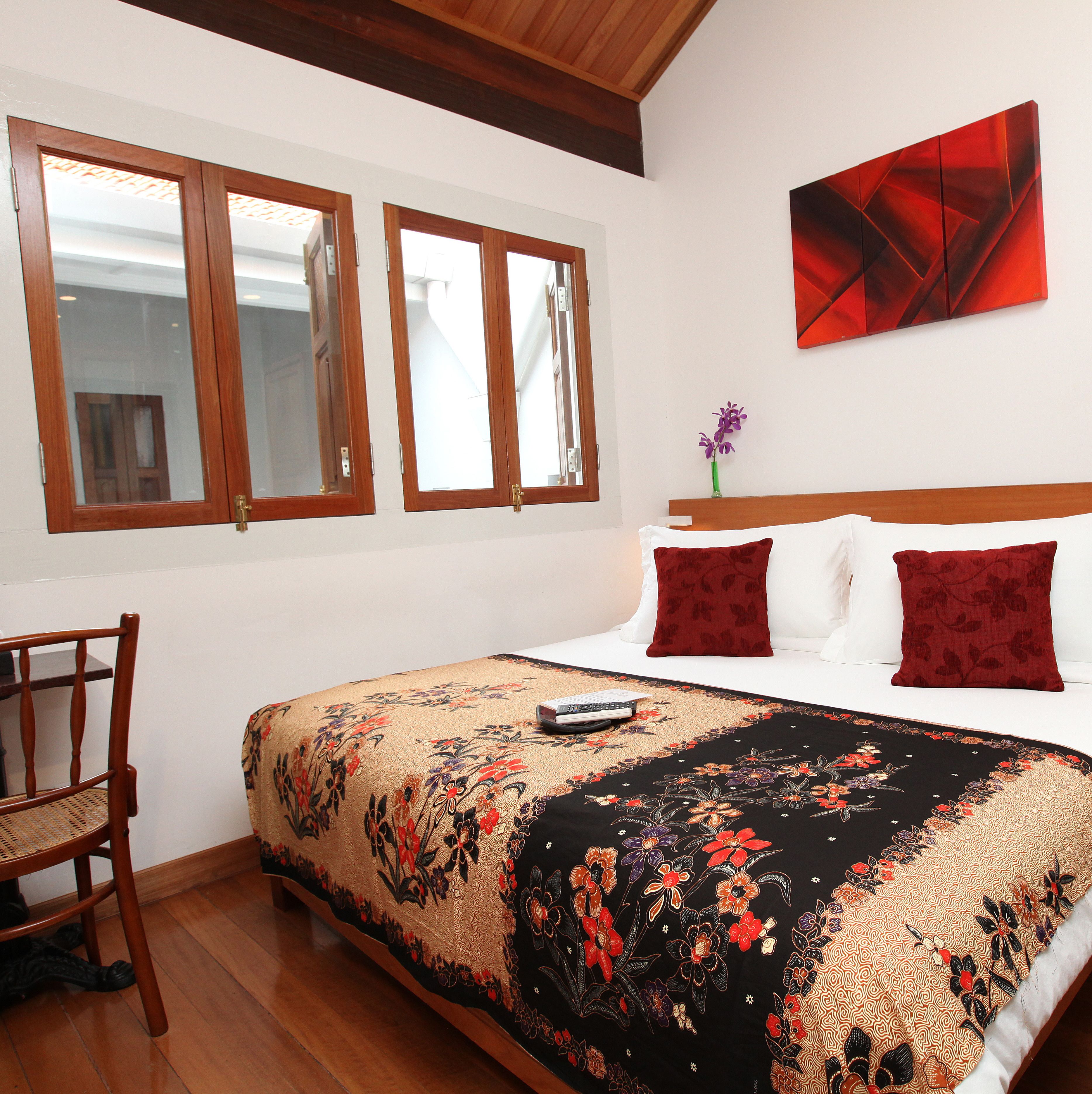 A bedroom with a bed, two windows, a chair, and a painting on the wall.
