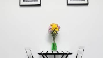 A dining area with a table and chairs, a vase with flowers, and two framed pictures on the wall.