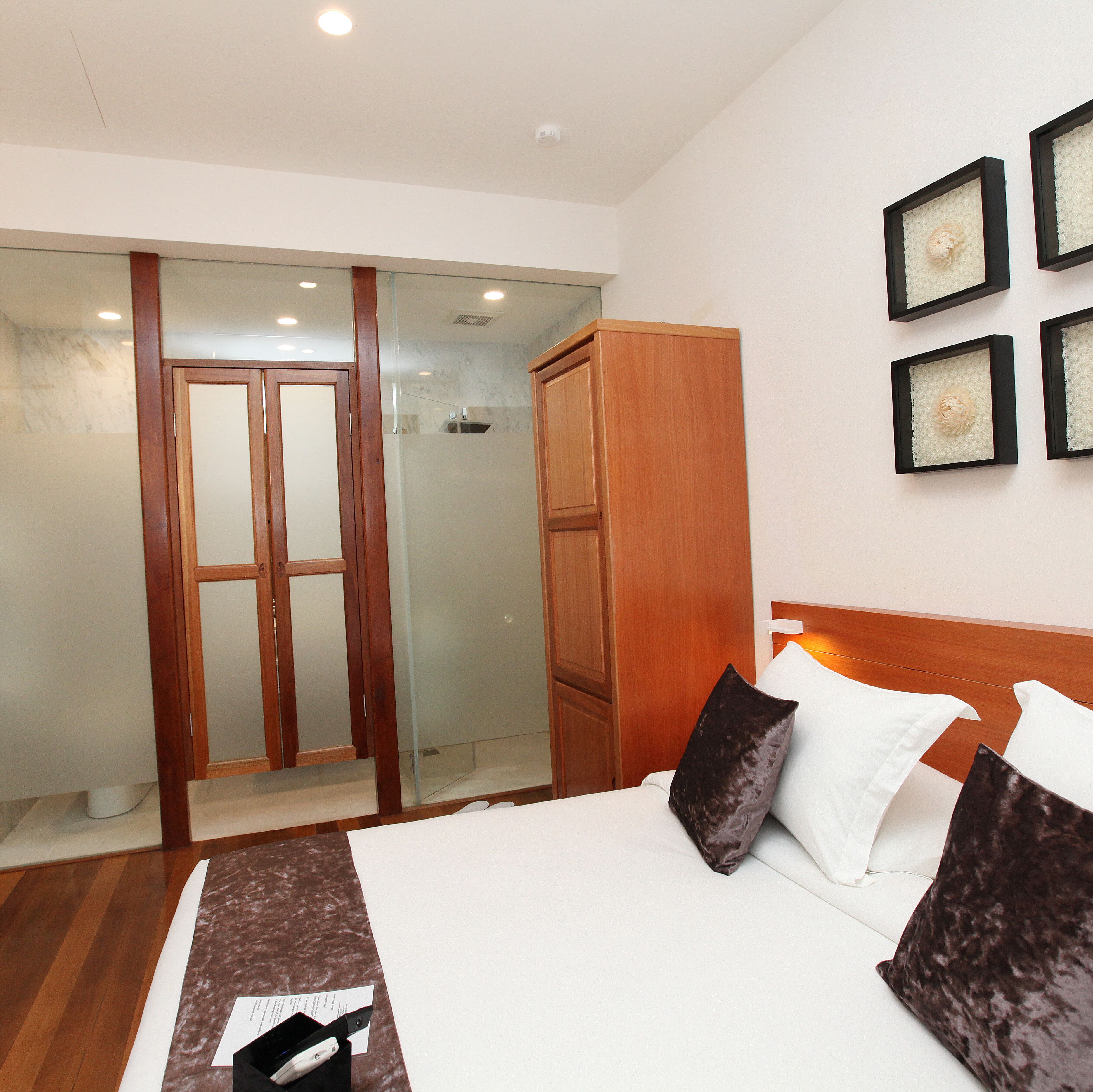 Une chambre d’hôtel avec un lit, une armoire en bois, une douche en verre et des œuvres d’art encadrées accrochées au mur.
