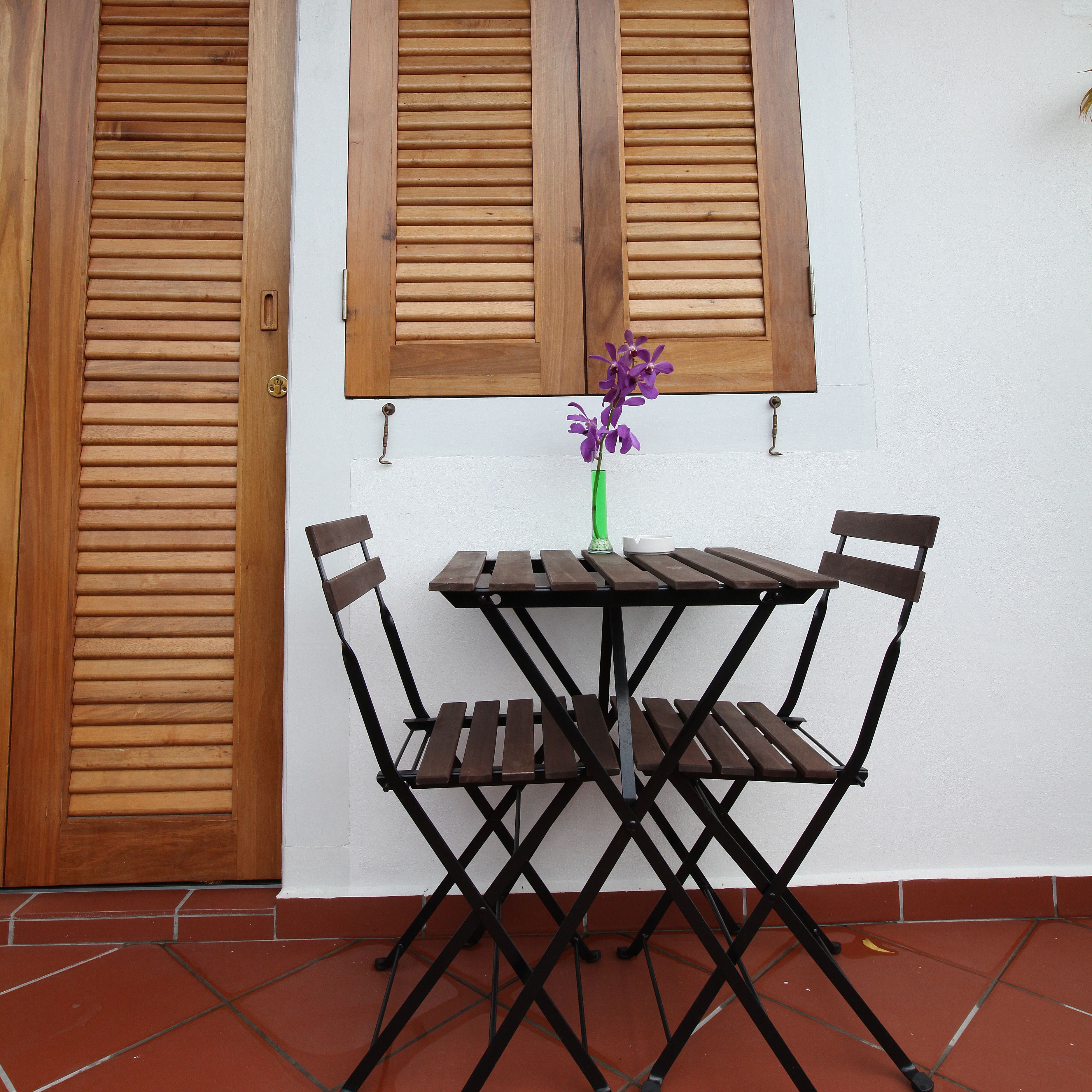 Ein Holztisch mit vier Stühlen, eine grüne Vase mit violetten Blumen und zwei Holztüren mit Fensterläden.