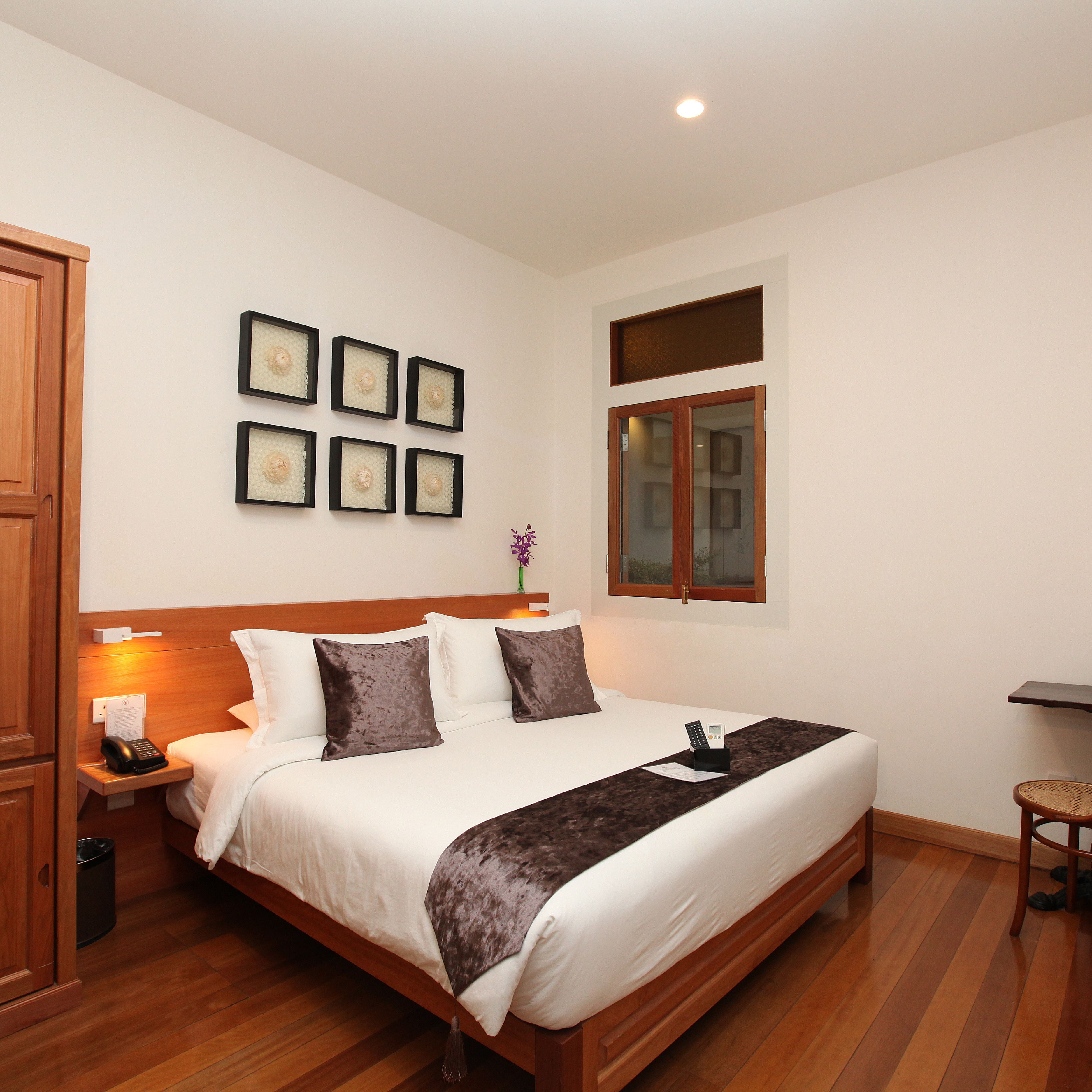 Una cama bien hecha con cabecera de madera, una mesita de noche con un teléfono y una lámpara. Seis cuadros enmarcados decoran la pared sobre la cama.