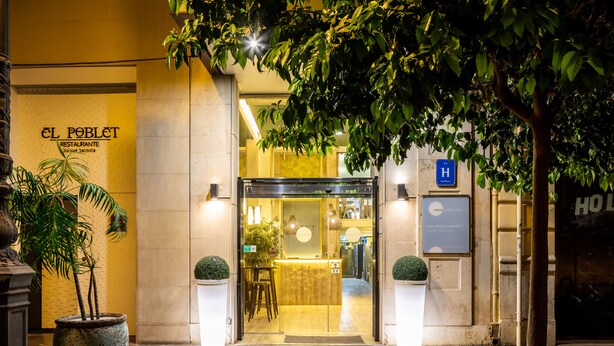 Der Eingang eines Hotels mit einer Rezeption, Blumentöpfen und einem sichtbaren Hinweisschild.