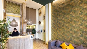 Ein Empfangsbereich mit Holztresen, hängenden Pendelleuchten, einem Sofa mit gelben Kissen und einer Wand mit Muster.