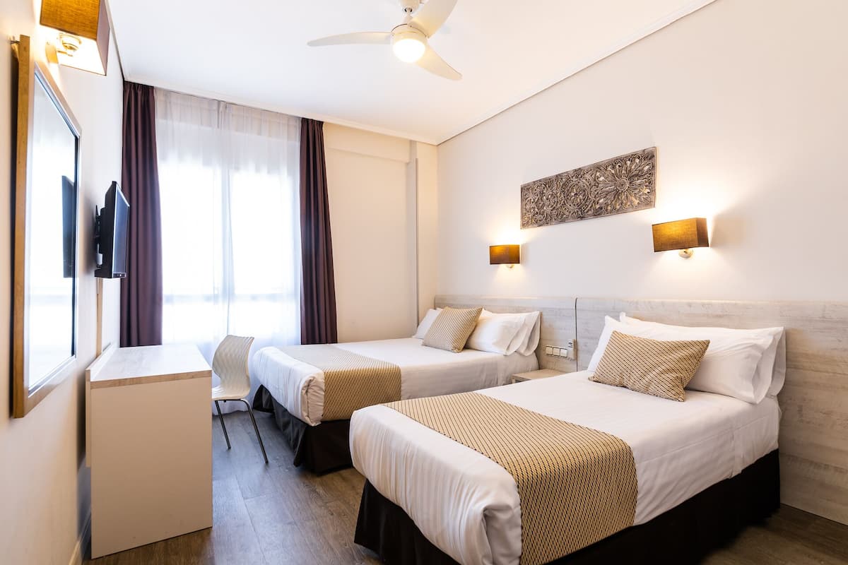 A hotel room with two beds, a desk, a chair, and a TV.