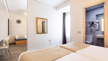 Habitació d'hotel amb dos llits, una taula de treball, una cadira, un mirall i un bany visible per una porta oberta.
