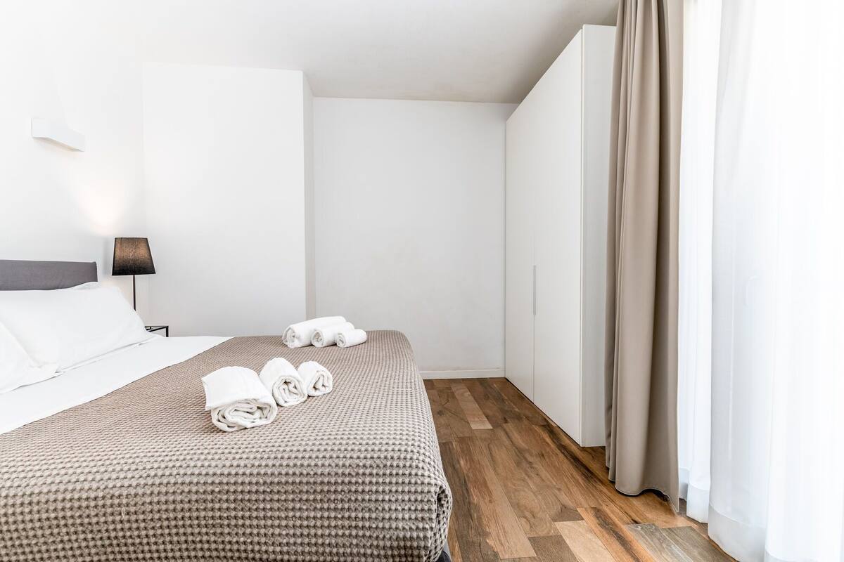 A hotel room with a bed, a nightstand, a lamp, and a window with curtains.