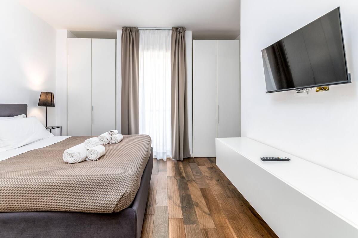 A modern hotel room with a bed, a TV mounted on the wall, and a wooden floor.