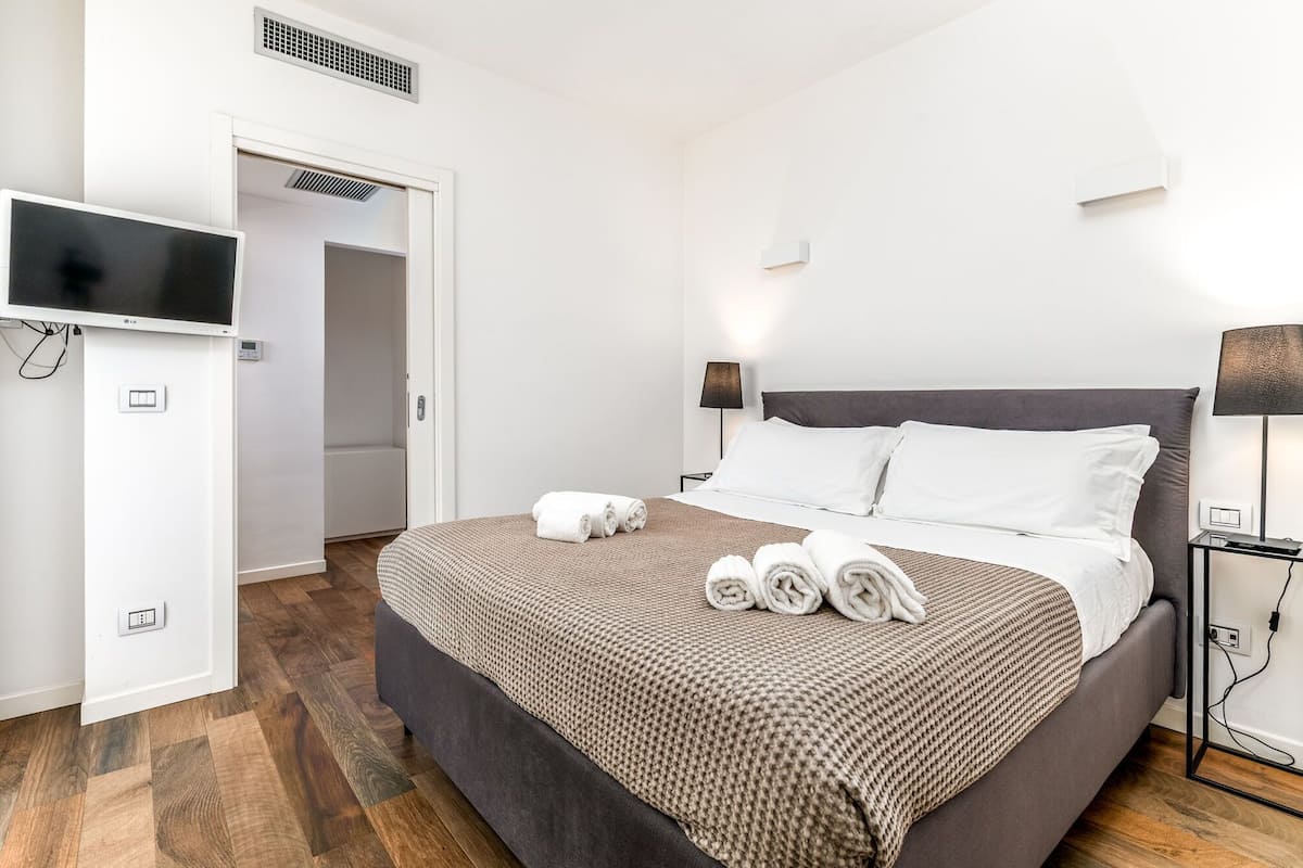 A hotel room with a bed, a TV, a lamp, and a wardrobe.