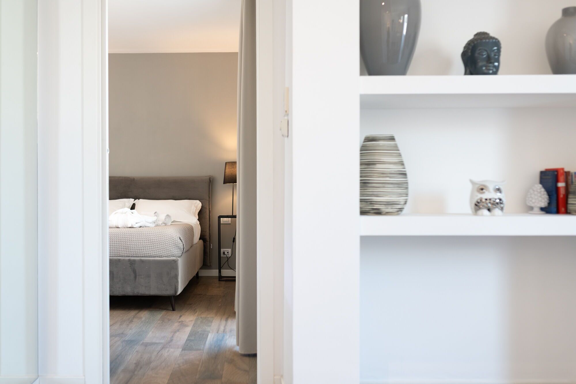 A bedroom with a bed, bedside table, lamp, and a shelf with decorative items.