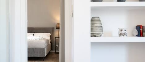 A bedroom with a bed, bedside table, lamp, and a shelf with decorative items.
