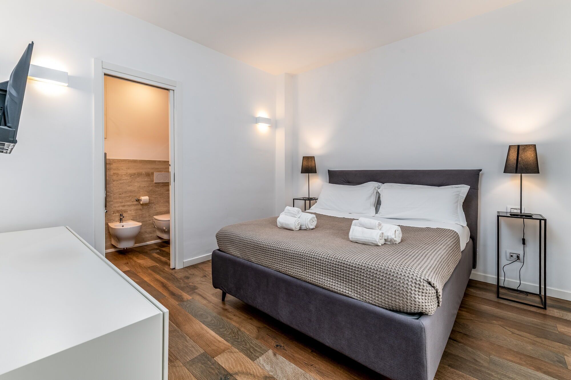 Habitación de hotel moderna con una cama grande, lámparas de noche, mesitas de noche y vistas al baño.