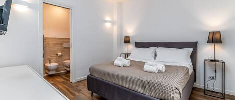 Habitación de hotel moderna con una cama grande, lámparas de noche, mesitas de noche y vistas al baño.