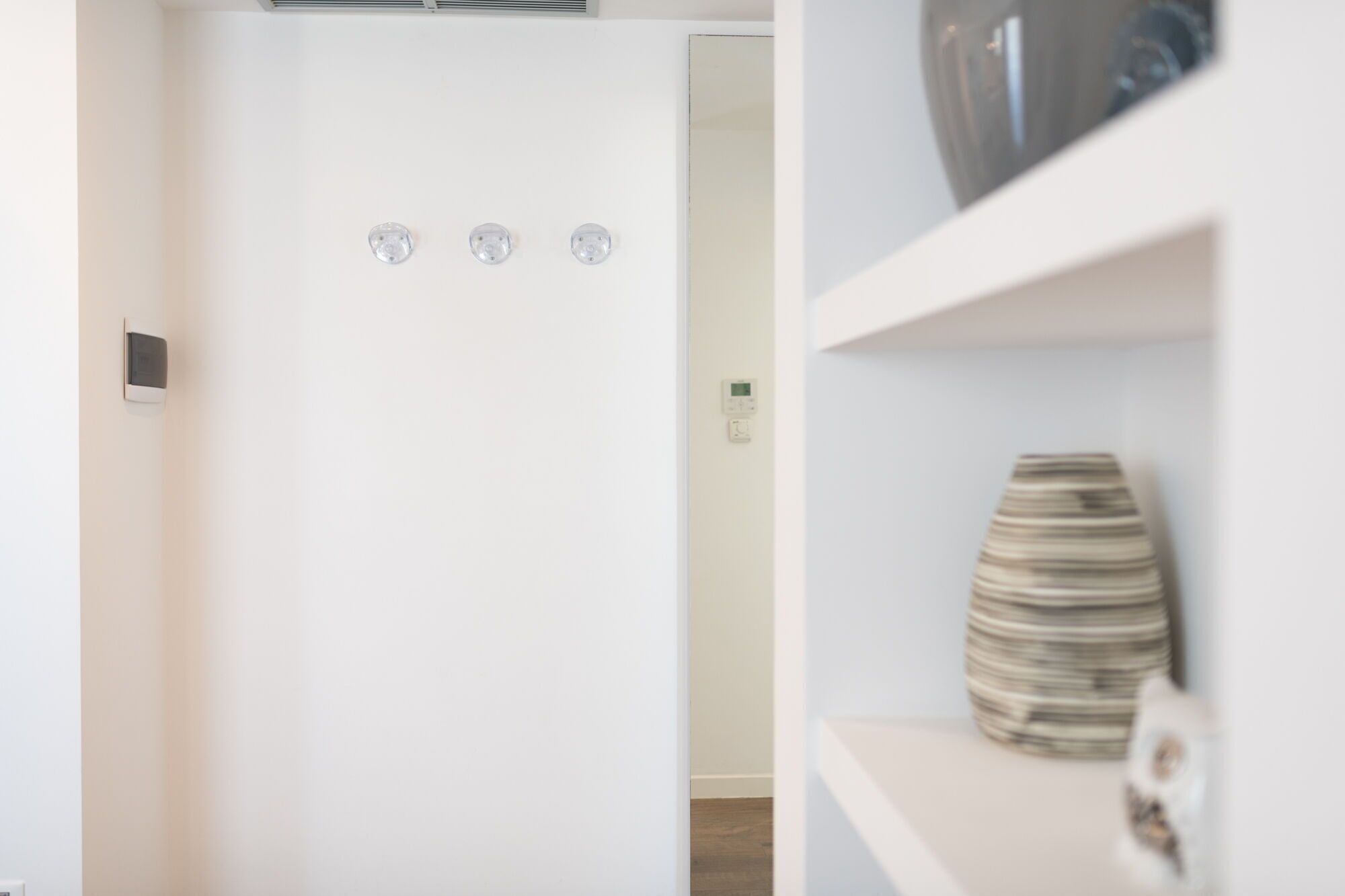 Une pièce moderne et minimaliste, avec une porte blanche, un thermostat fixé au mur et une étagère sur laquelle se trouve un vase à rayures.