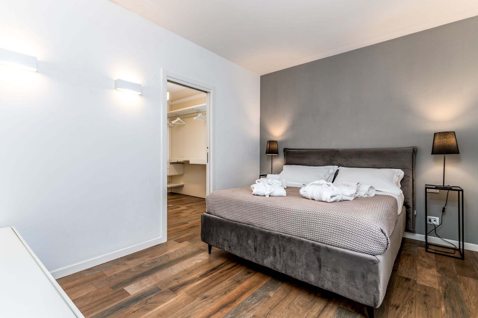 A modern bedroom with a large bed, two bedside lamps, and a walk-in closet.